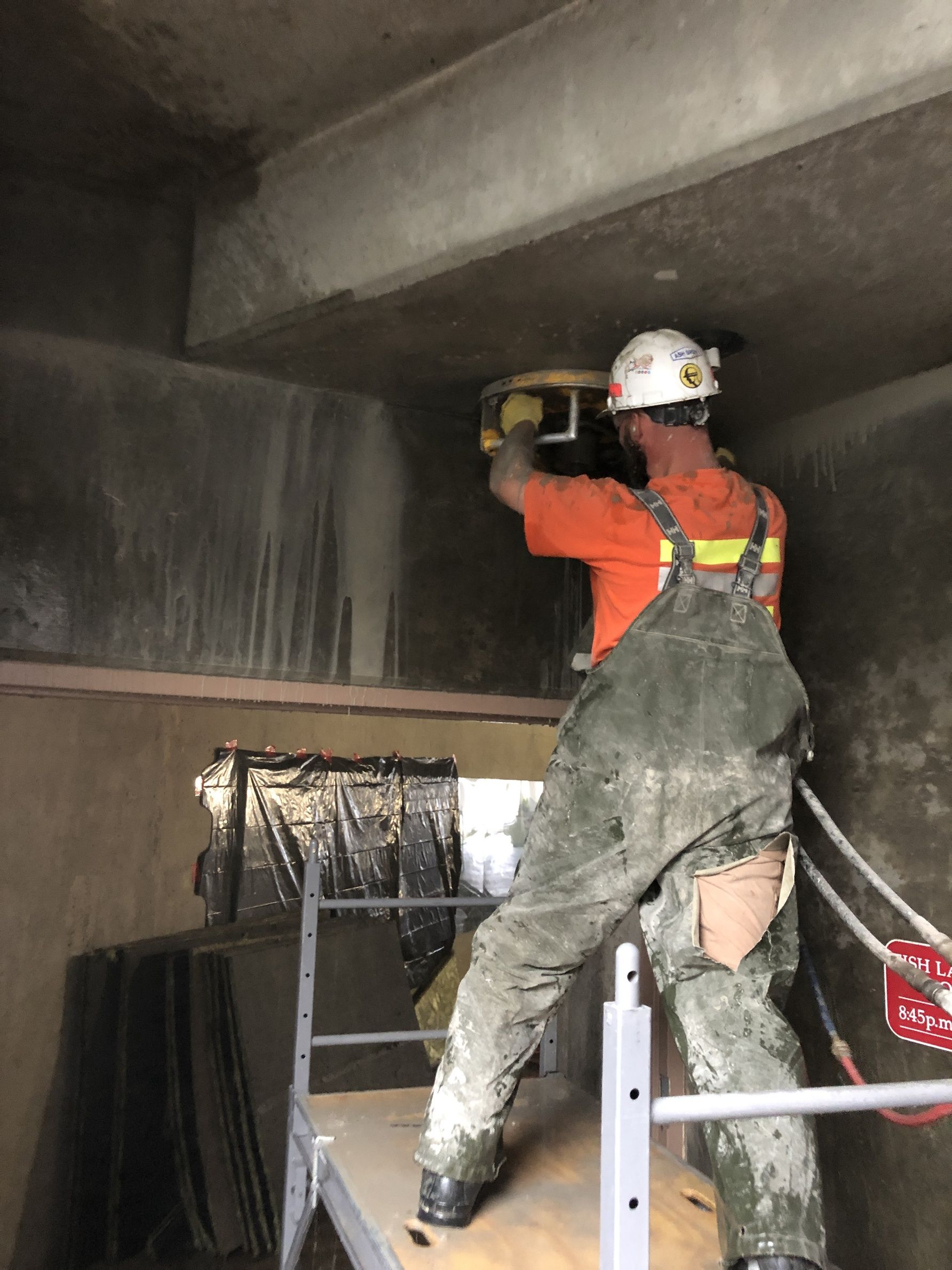 A man wearing a hard hat and overalls is standing on a scaffolding.