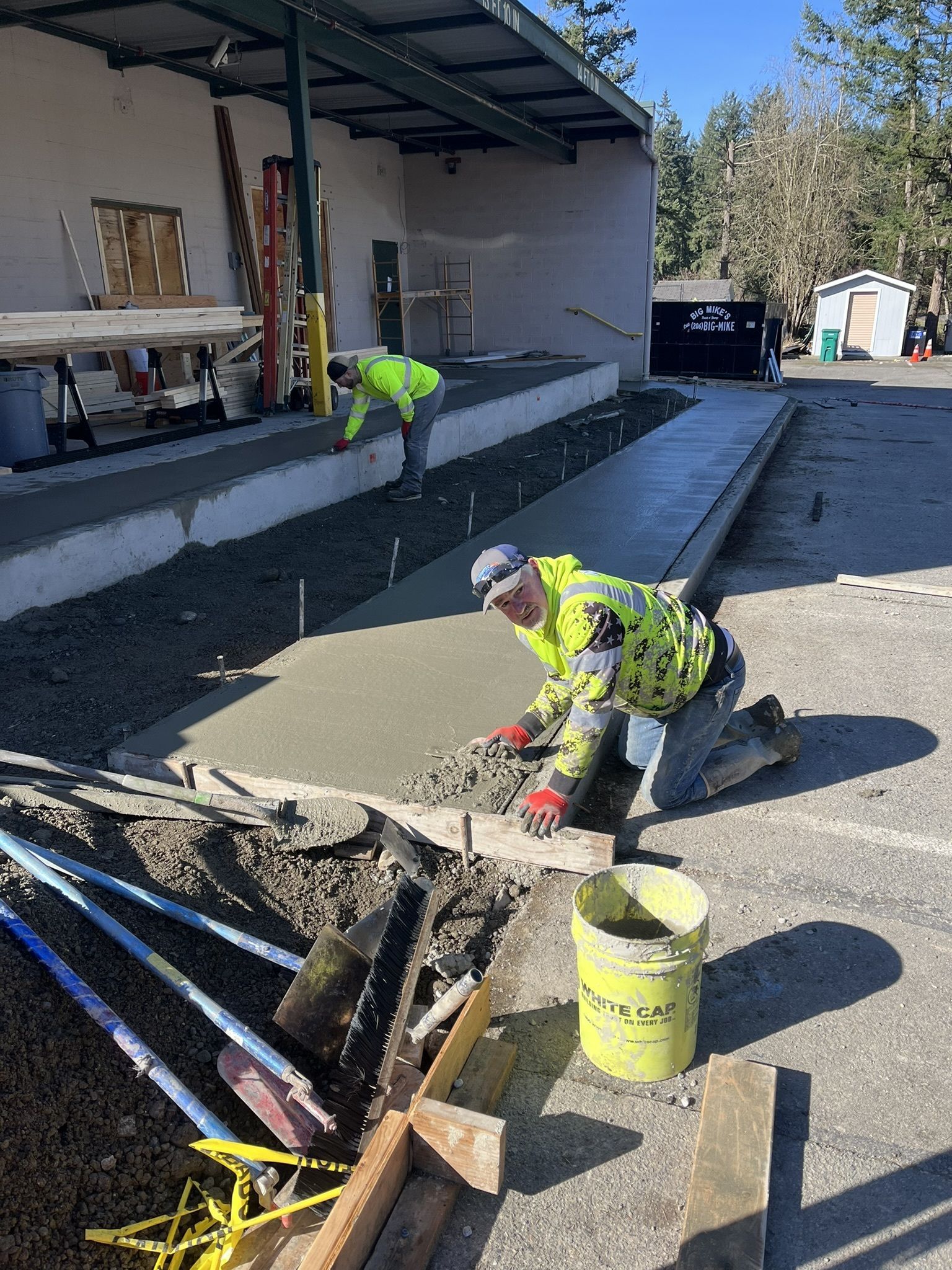 Two construction workers are working on a sidewalk in front of a building.