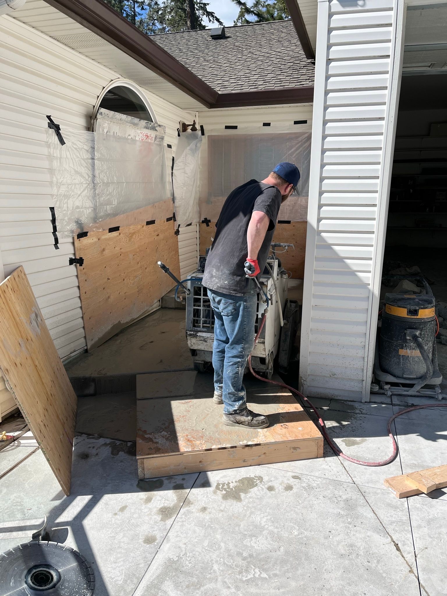 A man is standing in front of a garage door cutting concrete.