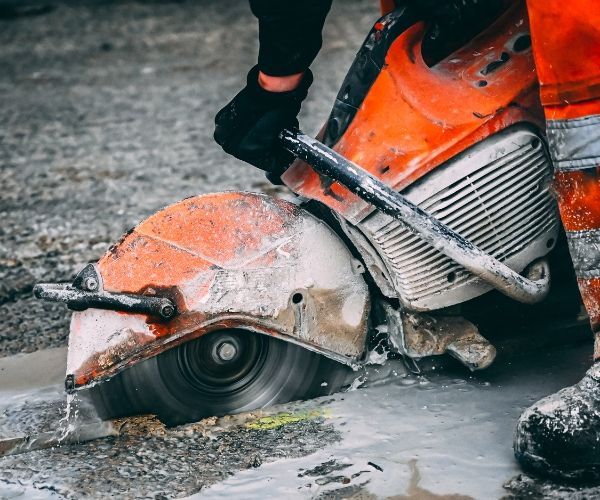 A person is using a concrete saw to cut a hole in the ground.