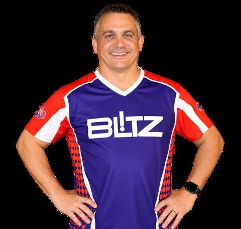 Smiling person in a purple and red BLITZ jersey, standing with hands on hips against a black background