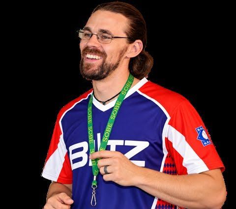 Smiling person in a blue, red, and white sports jersey with a green lanyard on a black background