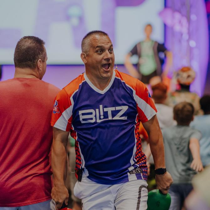 Smiling person in a purple and red BLITZ jersey, standing with hands on hips against a black background
