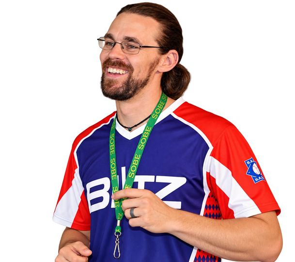Smiling person in a blue, red, and white sports jersey with a green lanyard on a black background