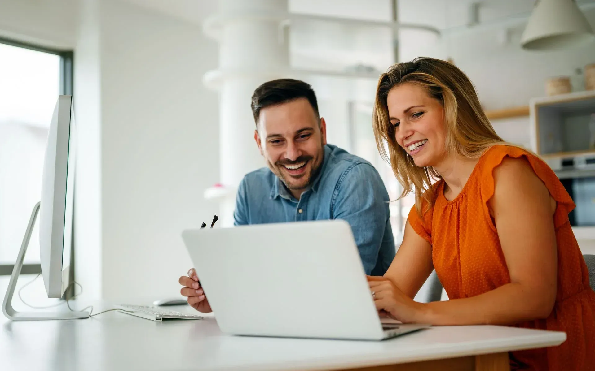 Een man en een vrouw zitten aan een tafel en kijken naar een laptopcomputer.