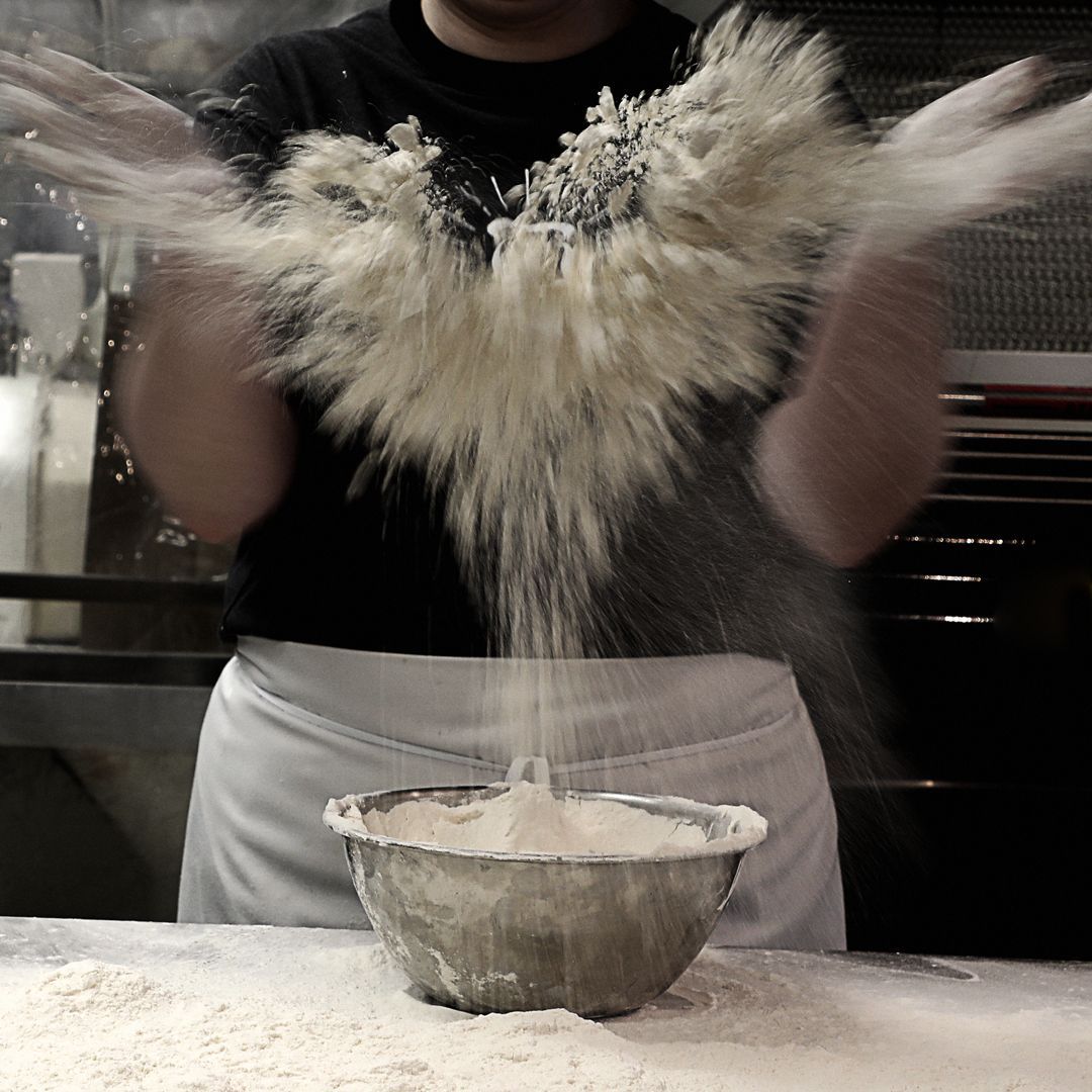 A person is throwing flour into a metal bowl