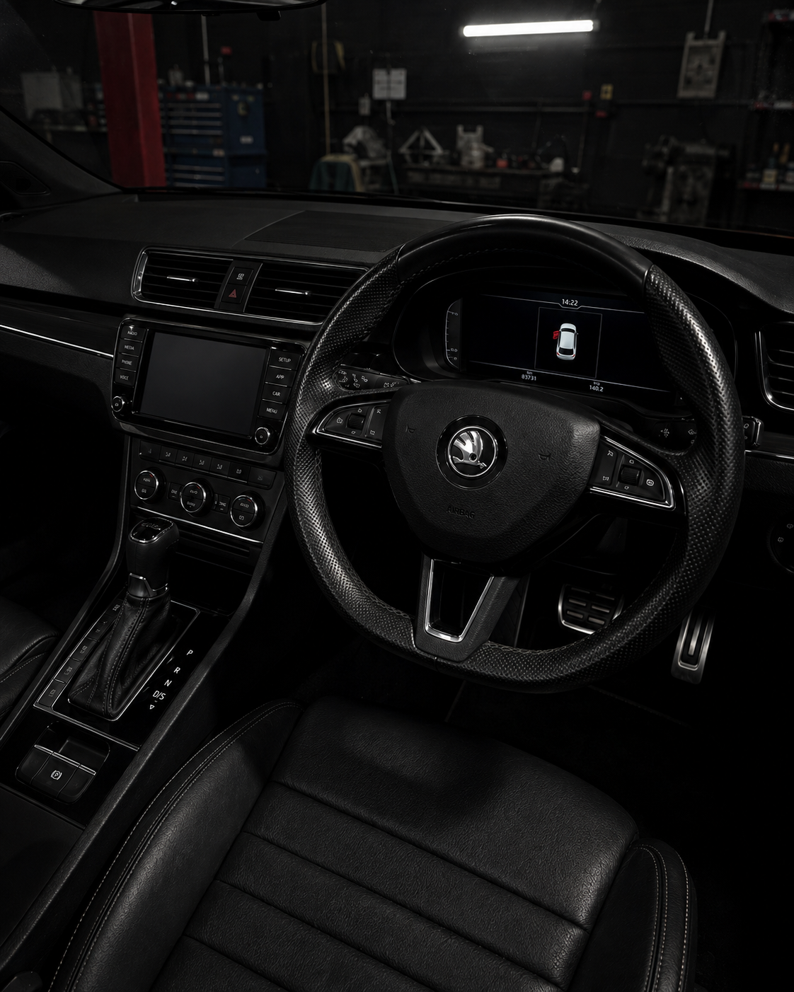 Dark car interior with black leather seats, steering wheel, dashboard, and center console in low light