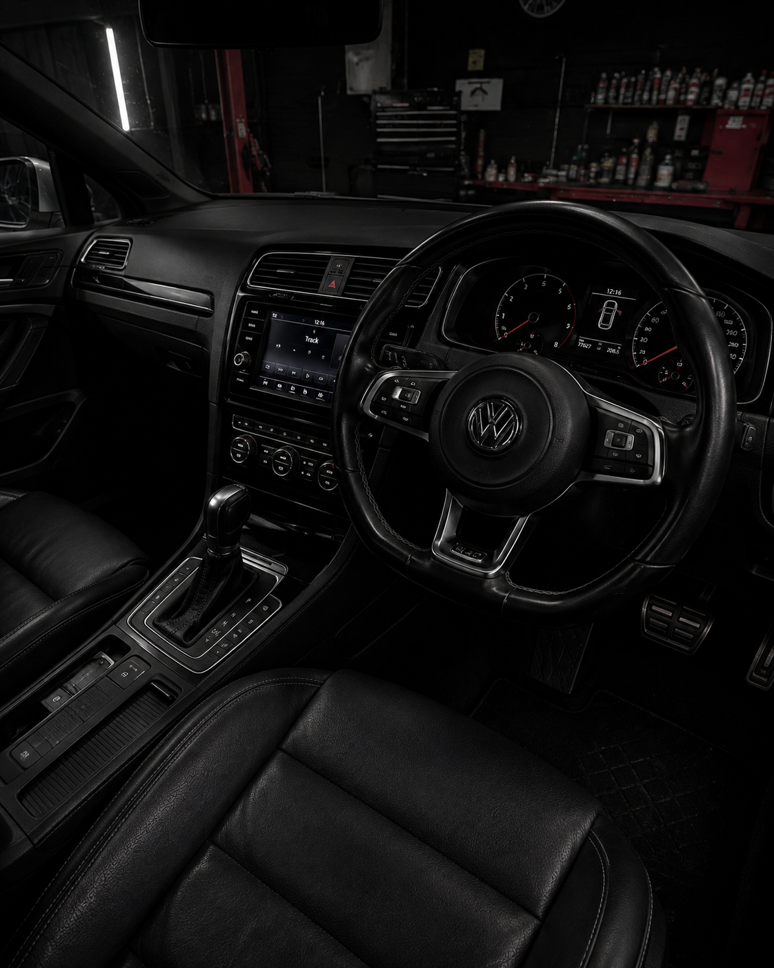 Dark car interior with steering wheel, dashboard, and center console in black leather.