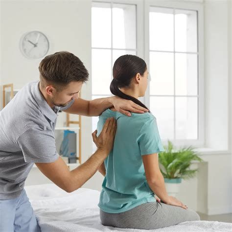 A man massages a woman's back in a light-filled room with a window and clock.