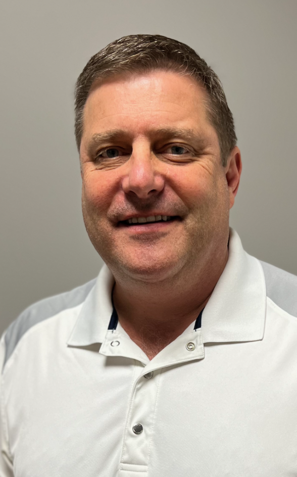 DR, Richard Whitney smiling, wearing a white polo shirt with gray shoulders, indoors.