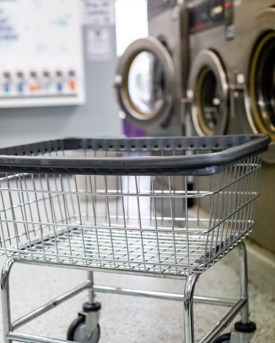 Wire laundry basket on a cart in a laundromat, with washing machines in the background