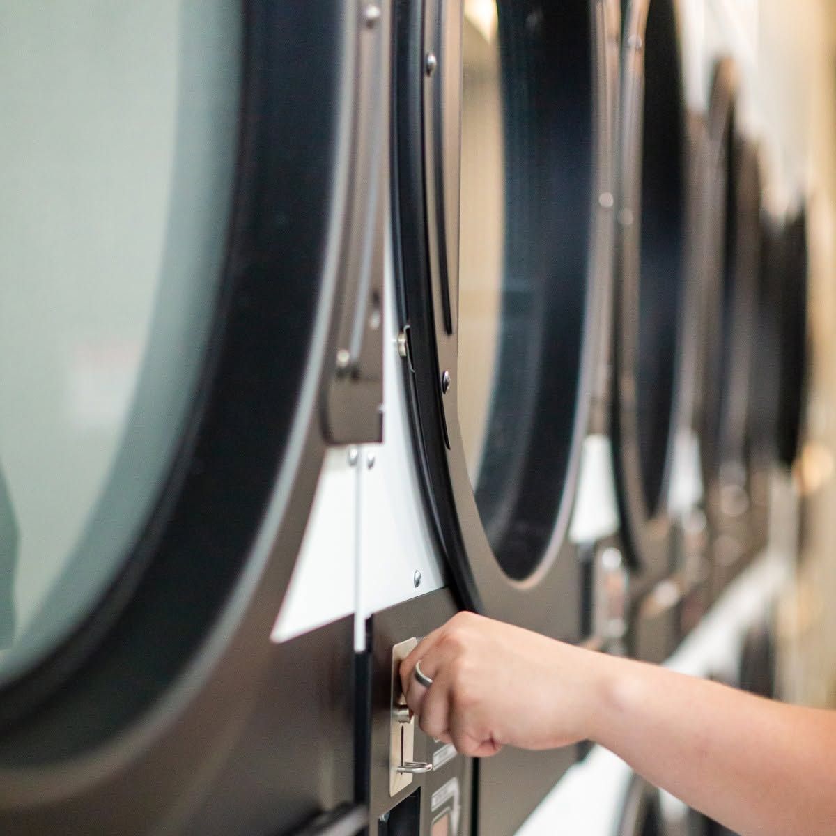 Hand placing a coin in a laundromat washing machine selector panel