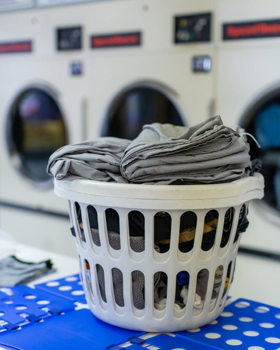 White laundry basket filled with folded gray clothes on a blue polka-dot surface in a laundromat