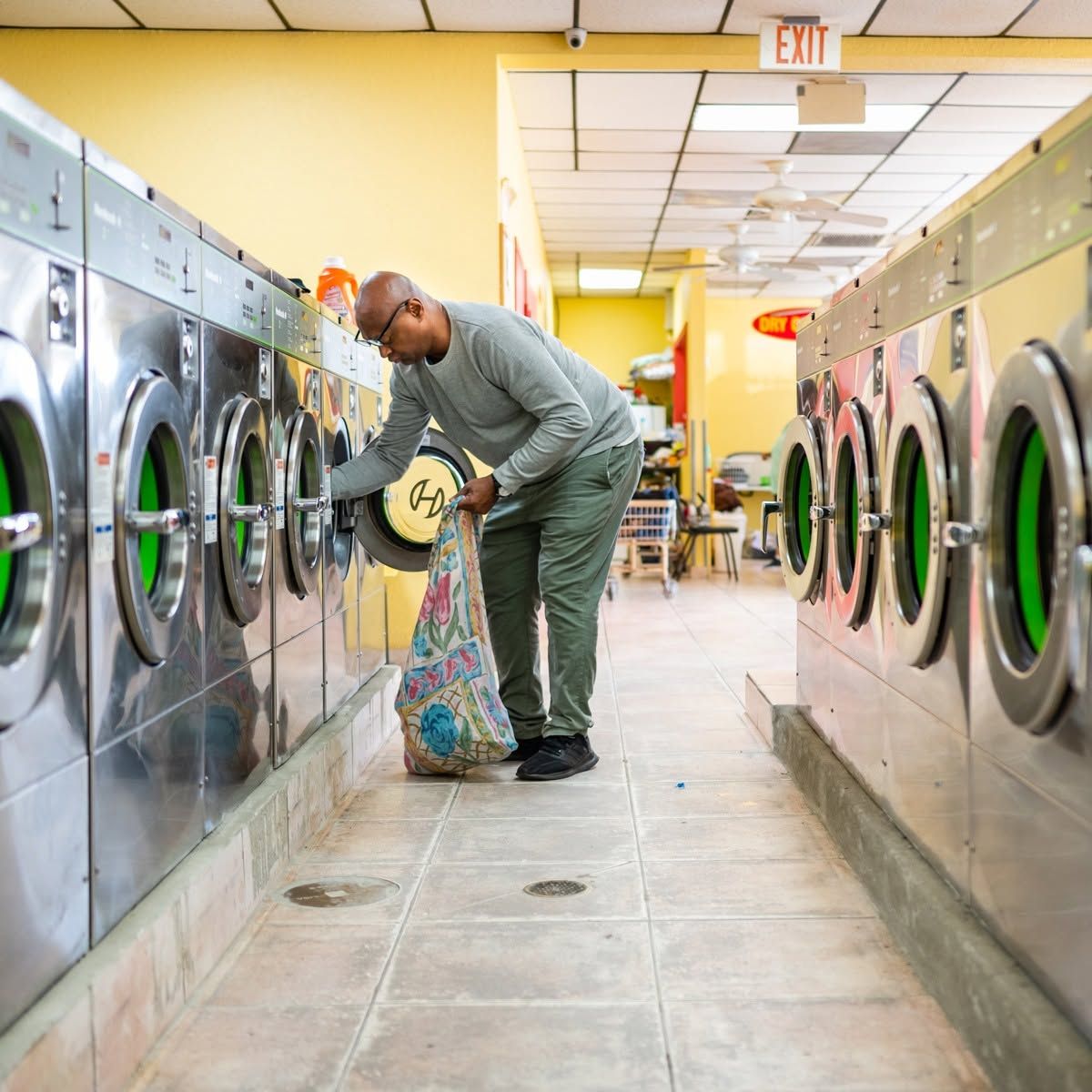 Person loading clothes into a washer in a brightly lit laundromat.