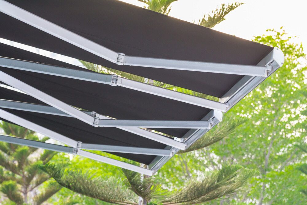 A Black Awning is Sitting Under a Tree in a Garden — Lismore Curtains & Blinds In Byron Bay, NSW