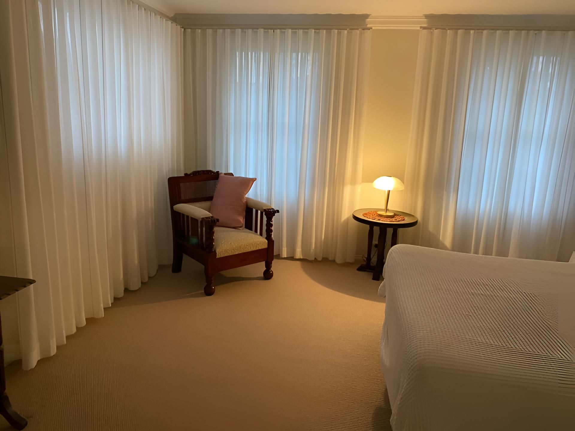 A Bedroom With a Bed, Chair, Table and Curtains — Lismore Curtains & Blinds In Byron Bay, NSW