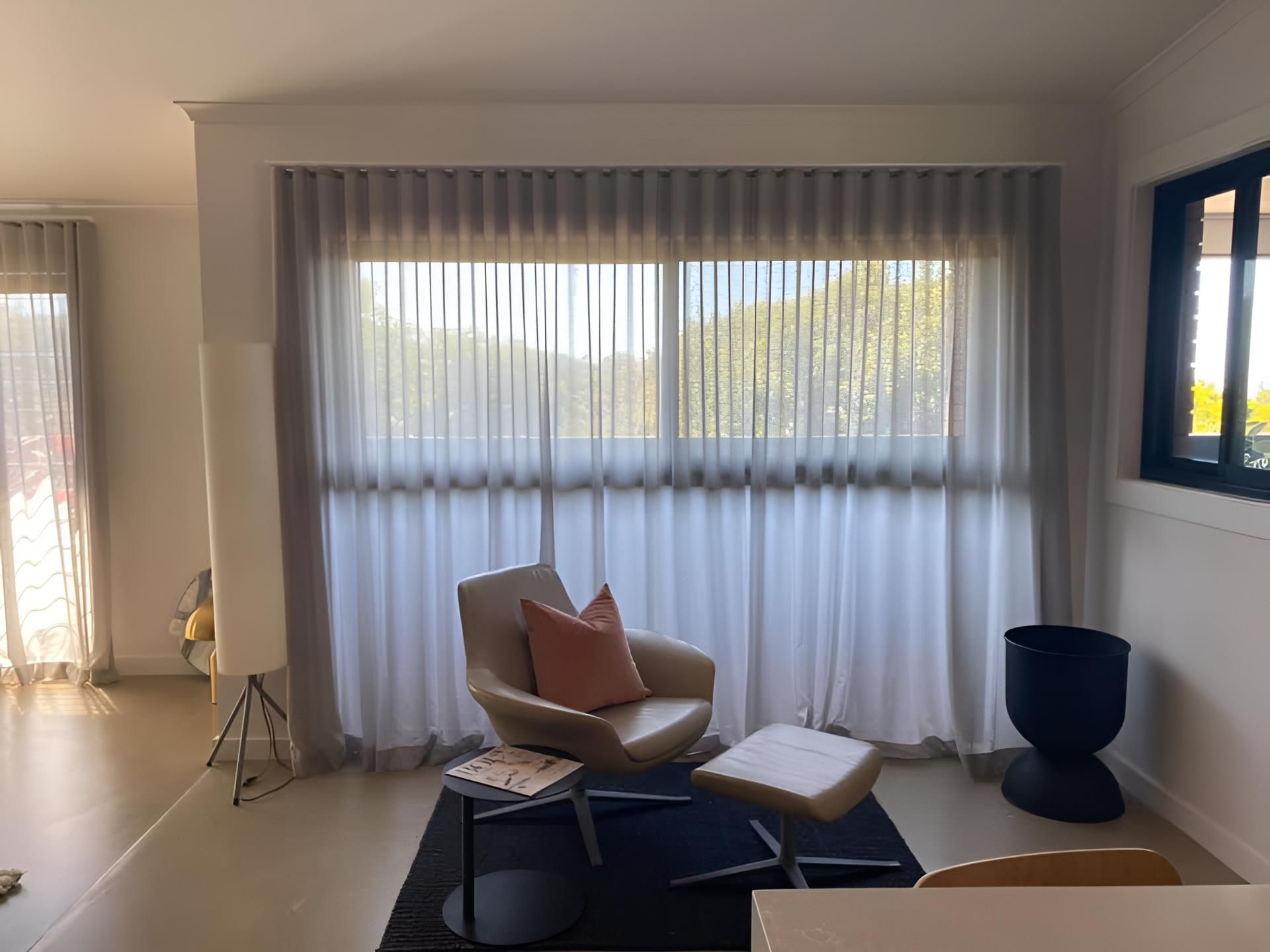 A Living Room With a Chair and Ottoman in Front of a Large Window — Lismore Curtains & Blinds In Lismore, NSW