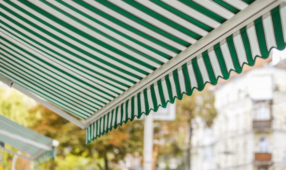 A Green and White Striped Awning is Hanging From the Roof of a Building — Lismore Curtains & Blinds In Ballina, NSW