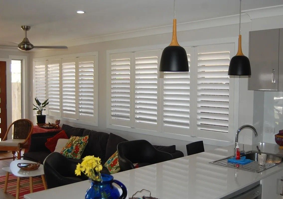 A Living Room With a Couch and a Kitchen With Shutters on the Windows — Lismore Curtains & Blinds In Lismore, NSW