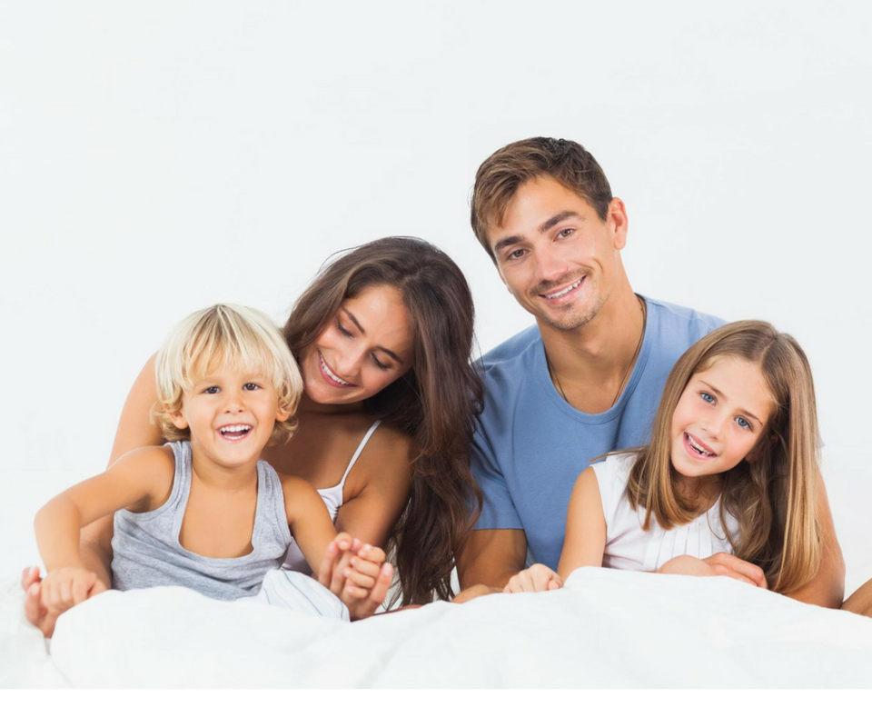 A family is laying on a bed together and smiling.