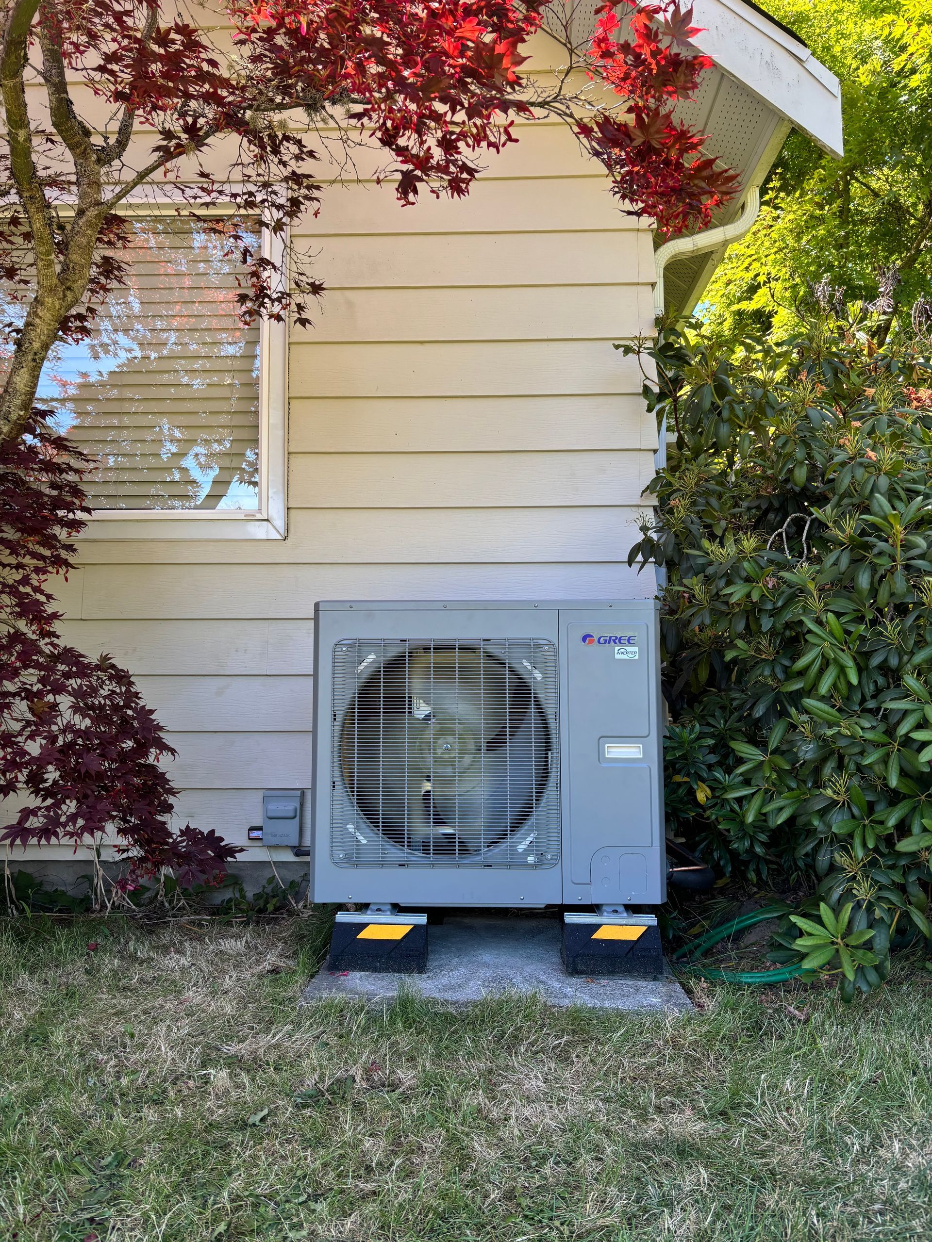 A heat pump is sitting on the side of a house.