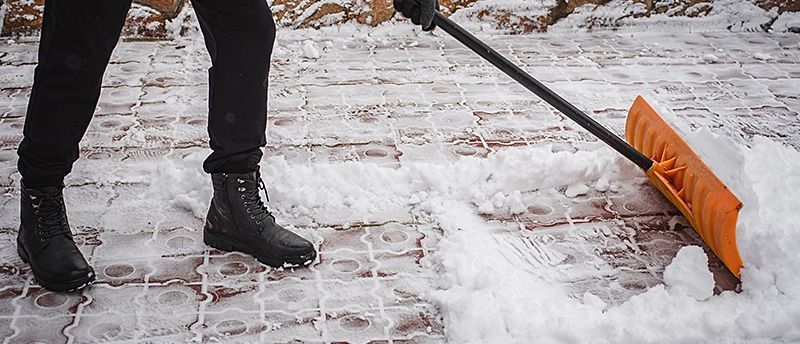 A person is shoveling snow on a brick sidewalk.