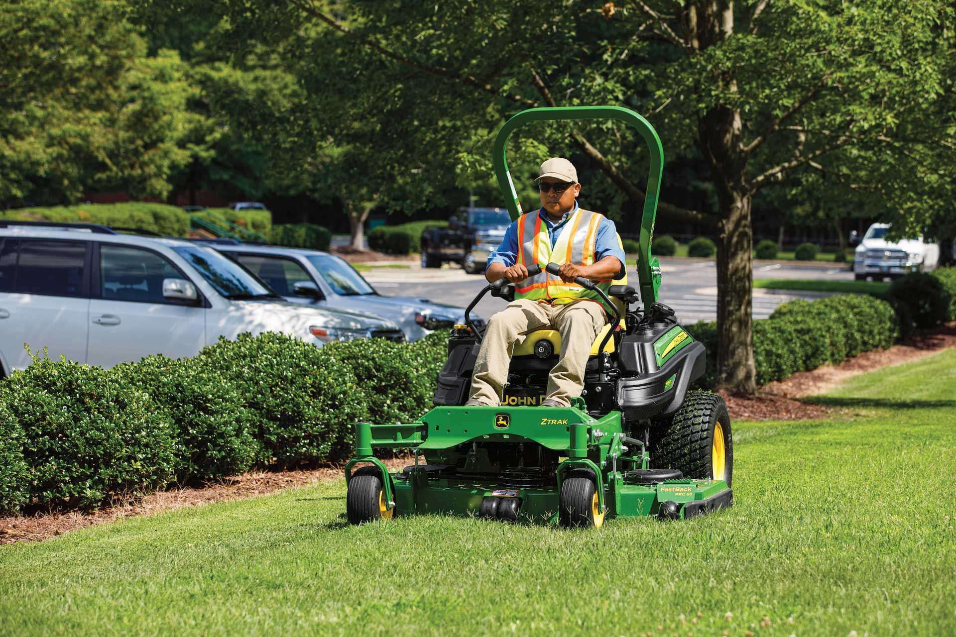 A man is riding a john deere lawn mower on a lush green lawn.