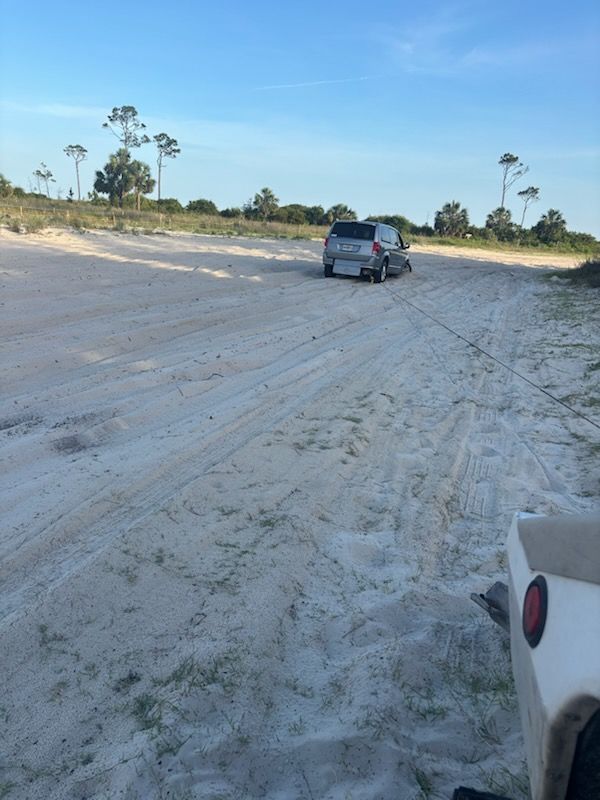 SUV driving on a sandy dirt road near sparse trees under a clear blue sky