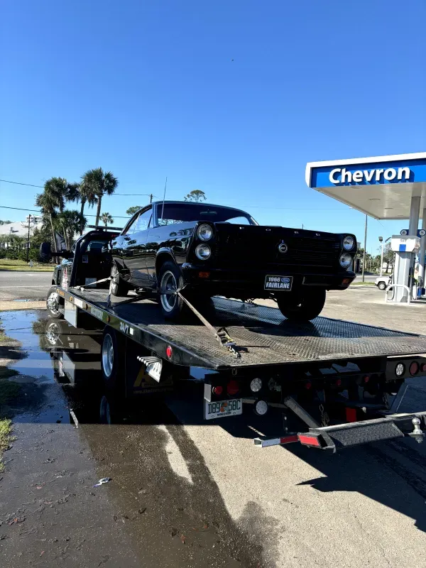 A black car is being towed to a chevron gas station