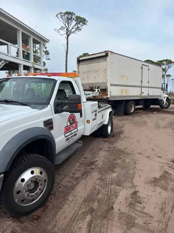 A white tow truck is towing a white semi truck.
