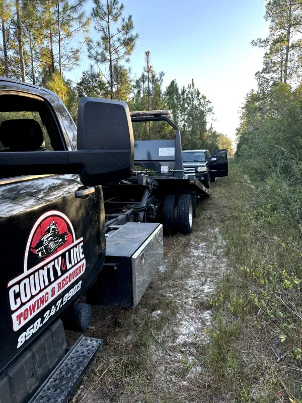 A county line towing truck is towing a car in the woods.