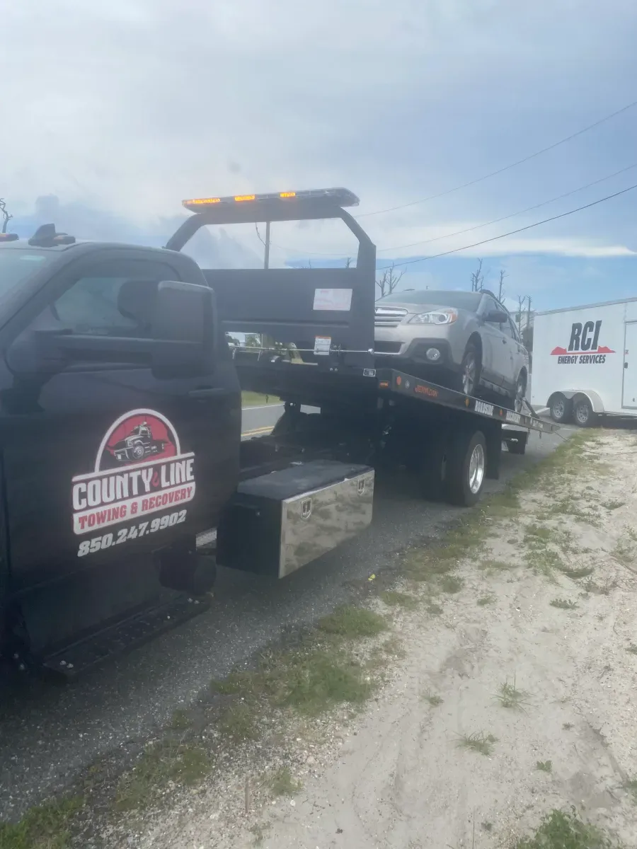 A tow truck is towing a car on the back of it.