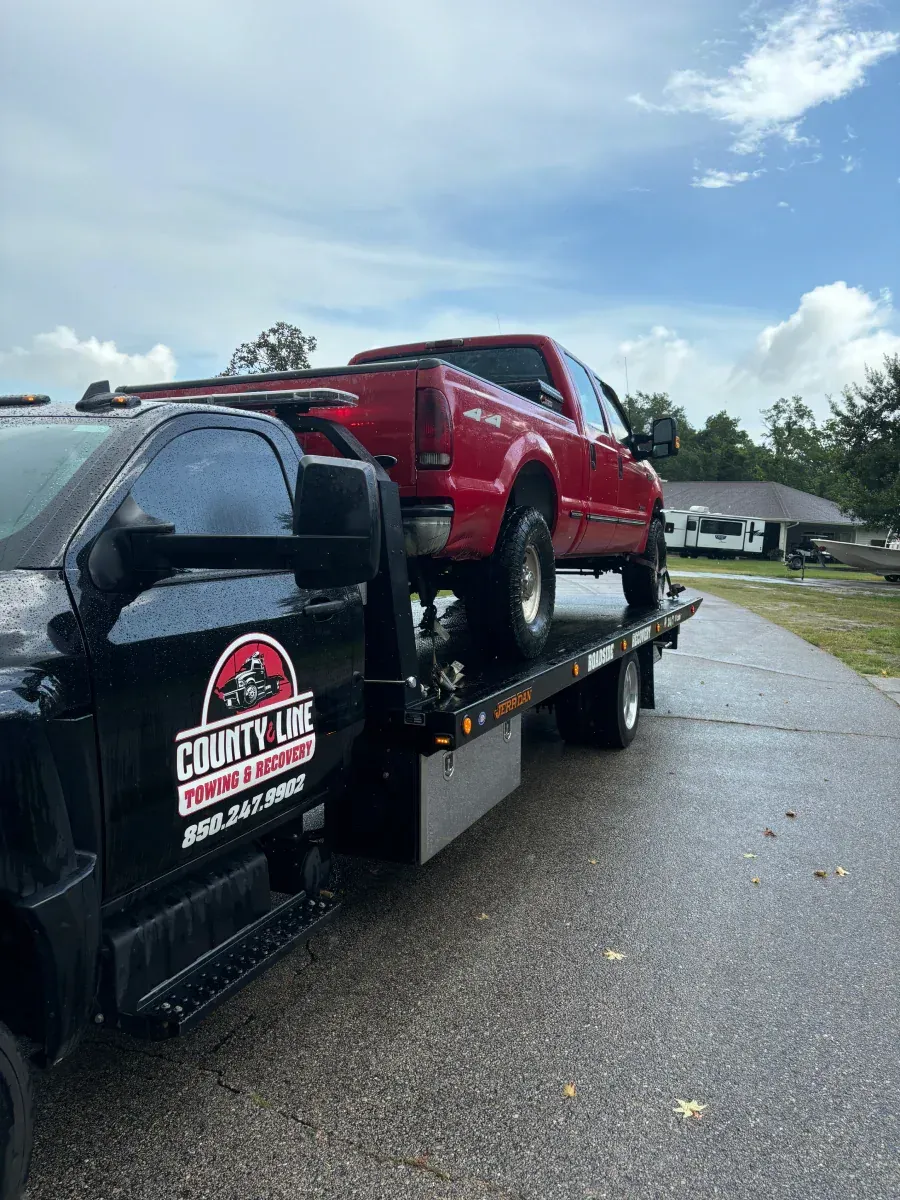 A red truck is being towed by a black tow truck.