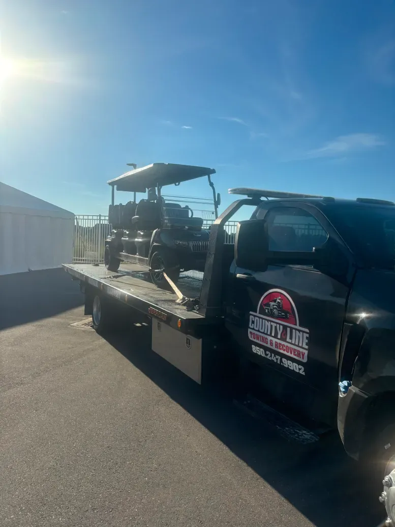 A tow truck with a golf cart on the back is parked on the side of the road.