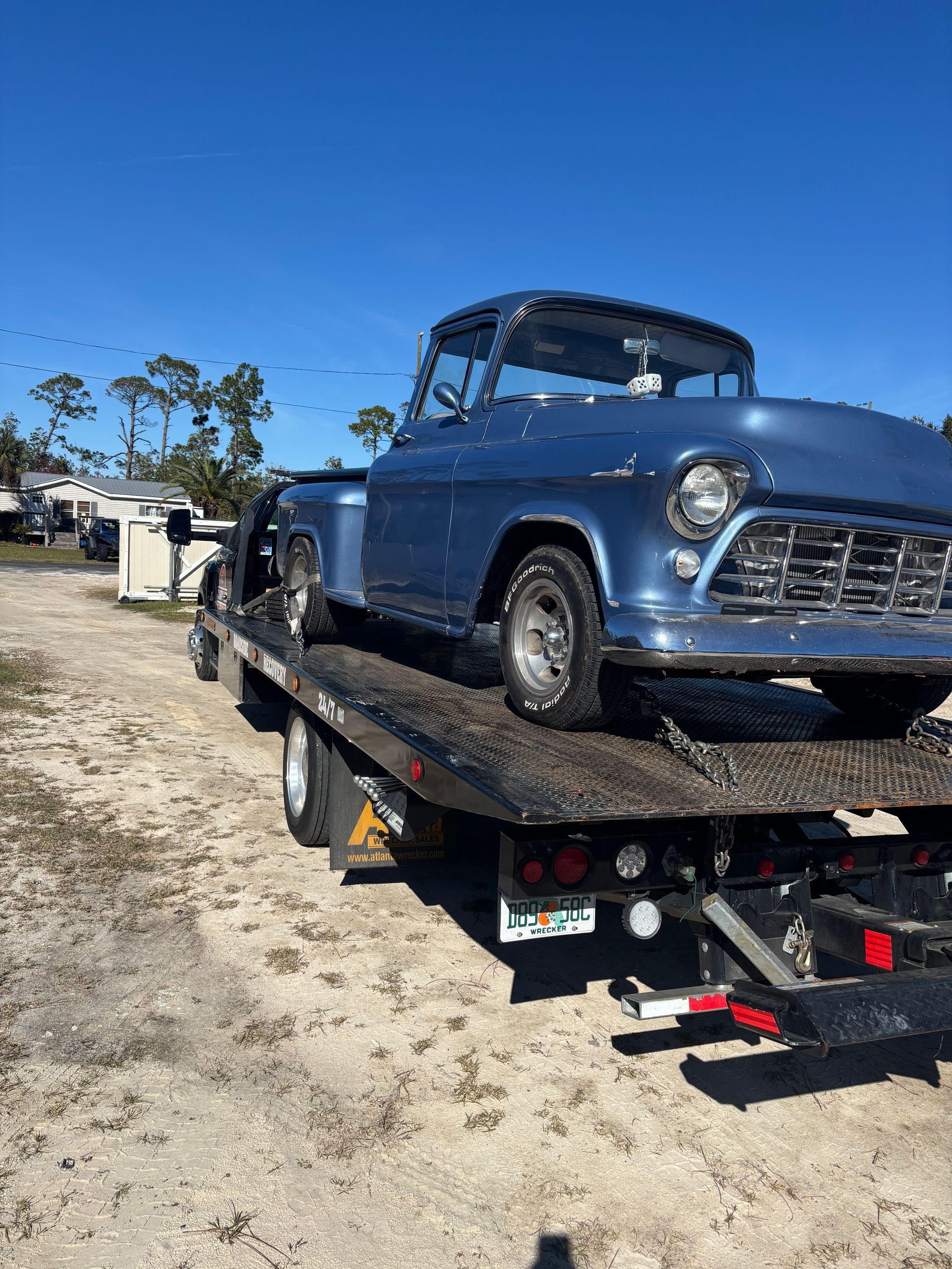 Blue classic pickup truck on a tow truck, outdoors on a sunny day.