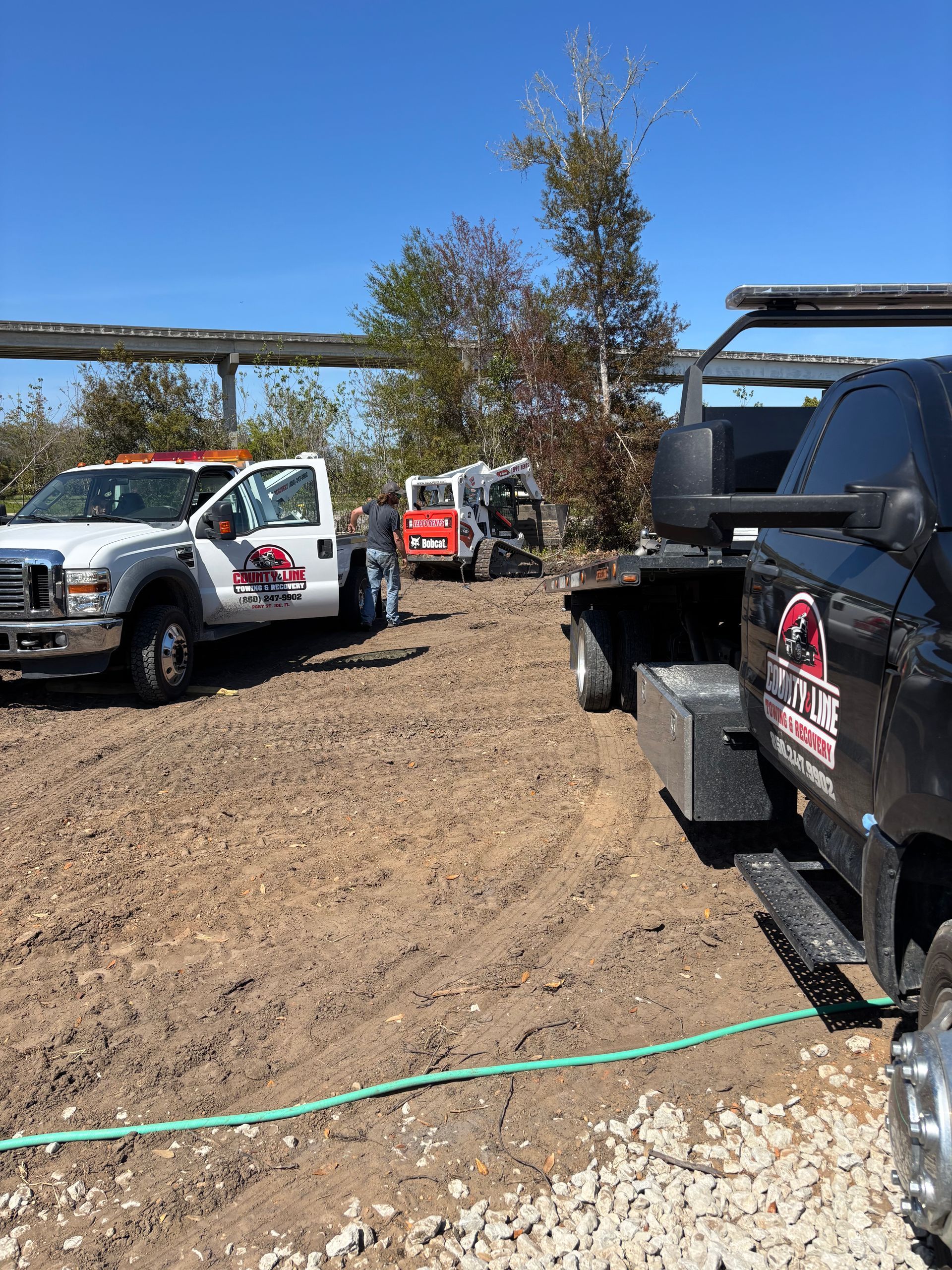 Tow trucks and construction equipment on a dirt lot under a blue sky.