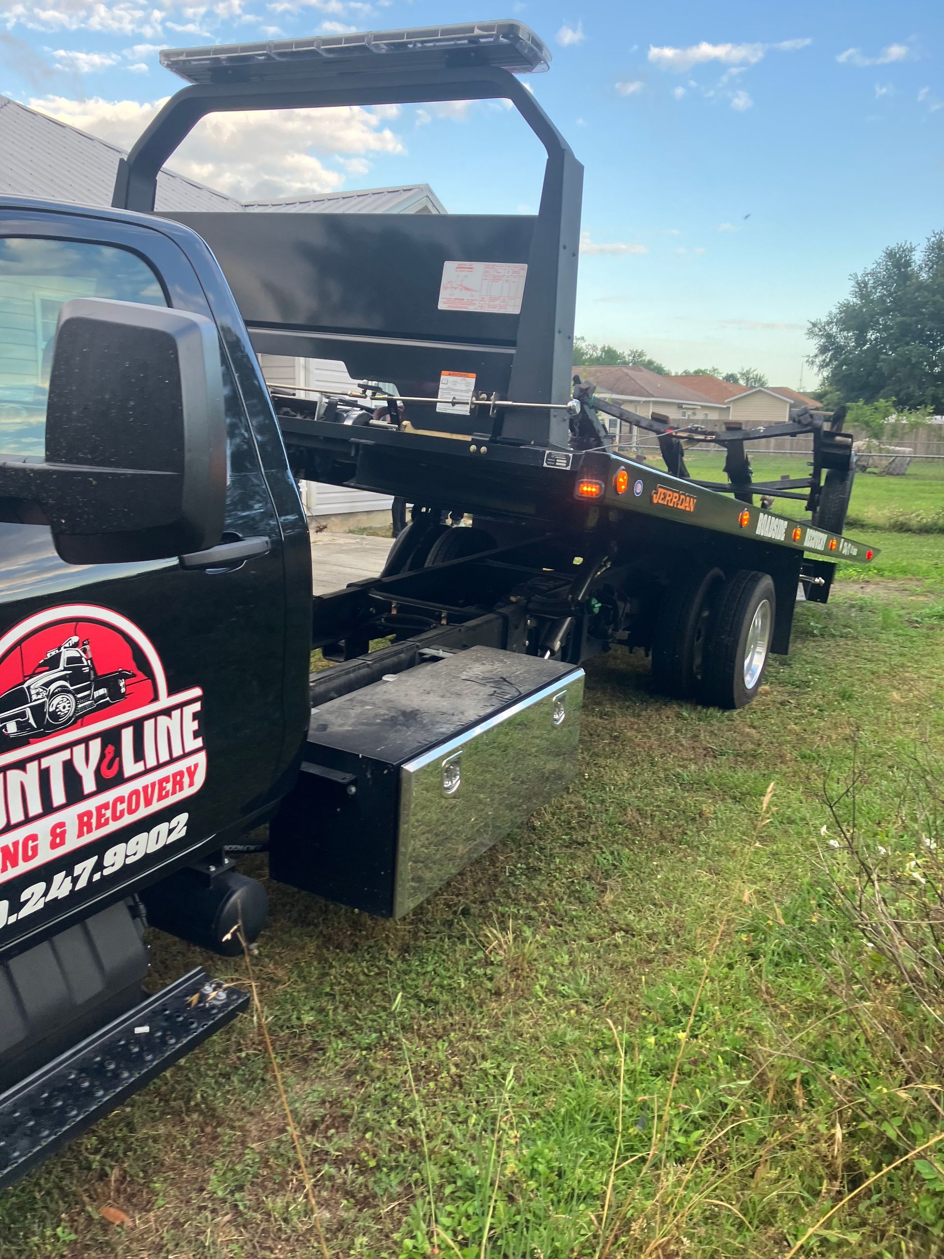 Black tow truck parked on grass with a black and red logo, blue sky in the background.