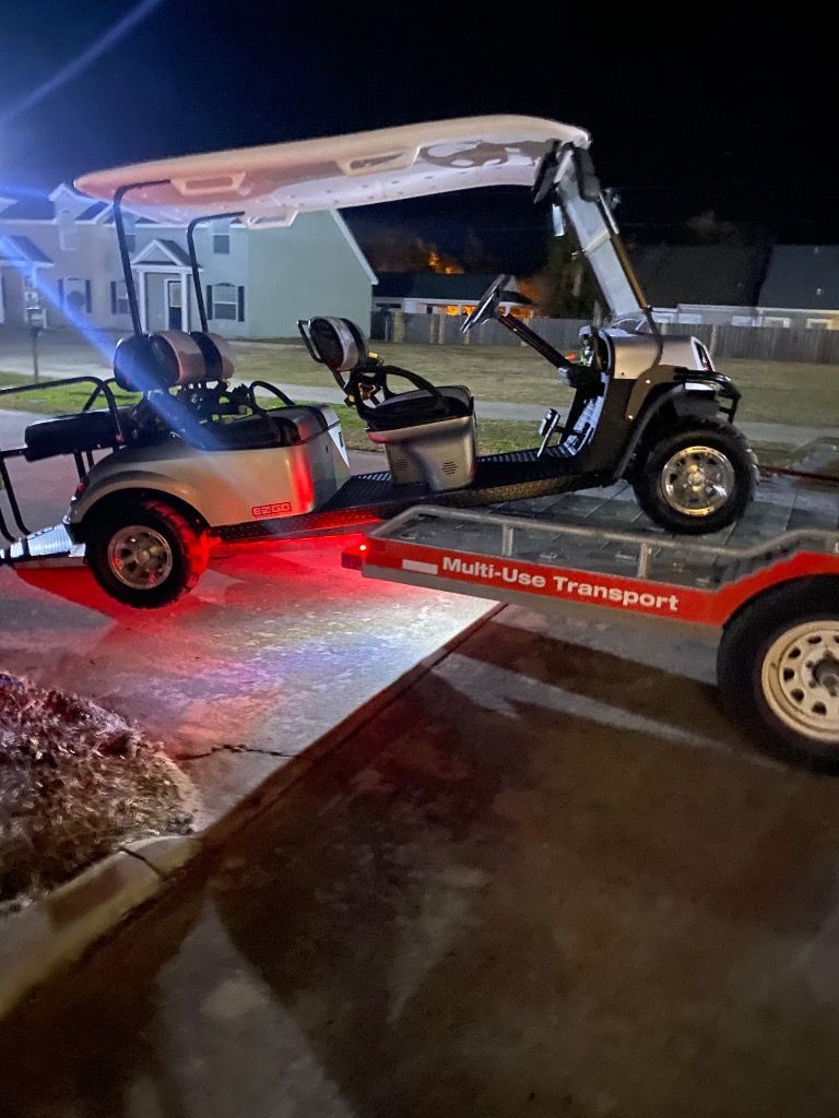 A light-colored golf cart with bright red underglow lighting is parked on a red utility trailer at night.