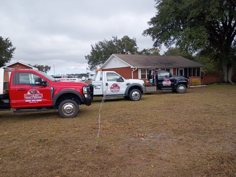 Three utility trucks parked on a grassy lot in front of a brick house under a cloudy sky.