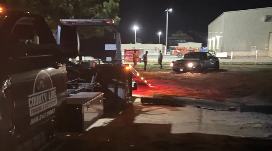 A tow truck is towing a truck in a parking lot at night.
