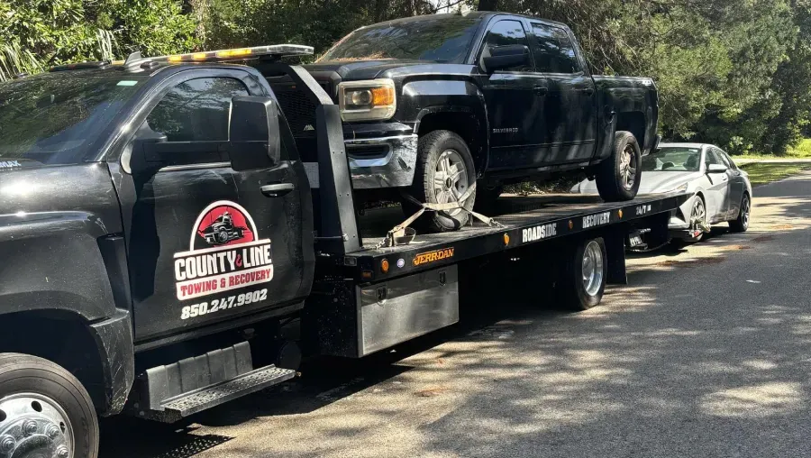 A tow truck is carrying a truck on the back of it.