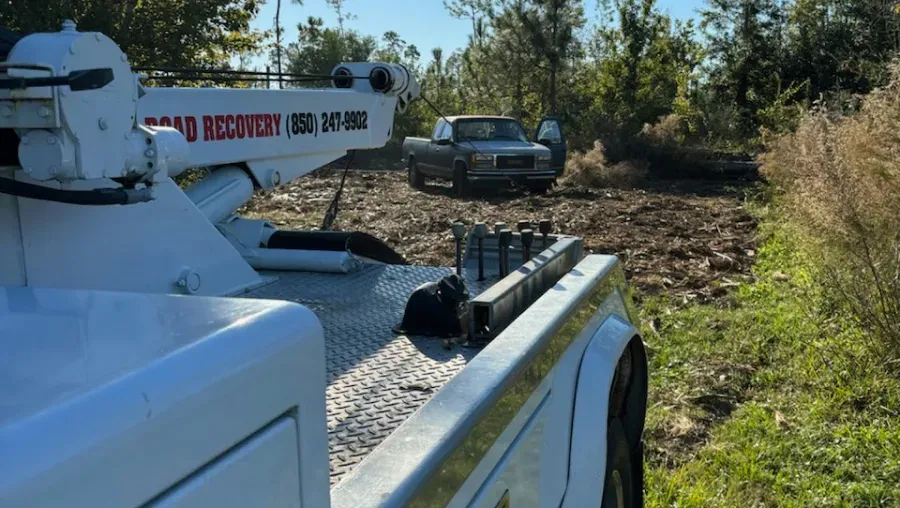 A white tow truck is parked on the side of a dirt road.