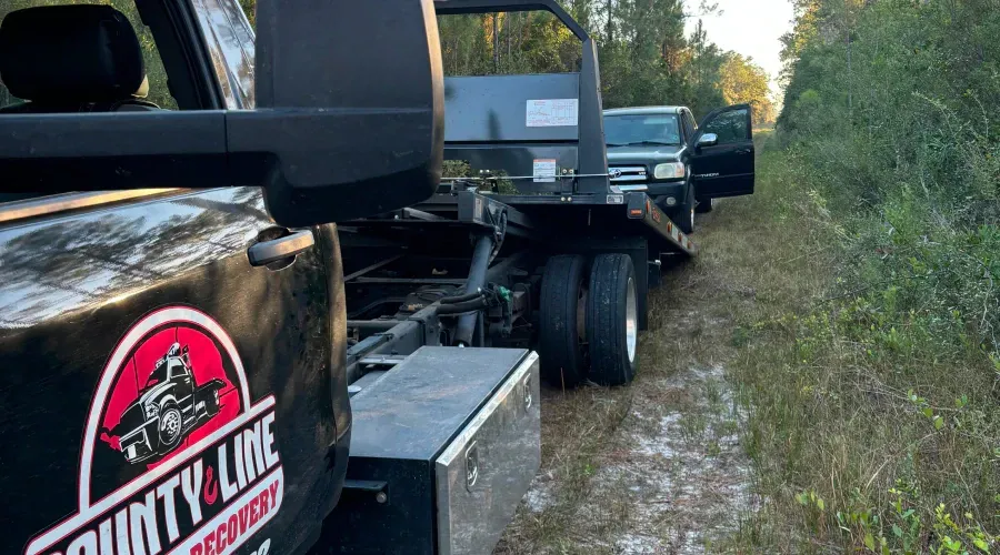A tow truck is towing a car in a muddy field.