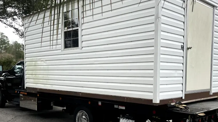 A small white house is being towed by a tow truck.