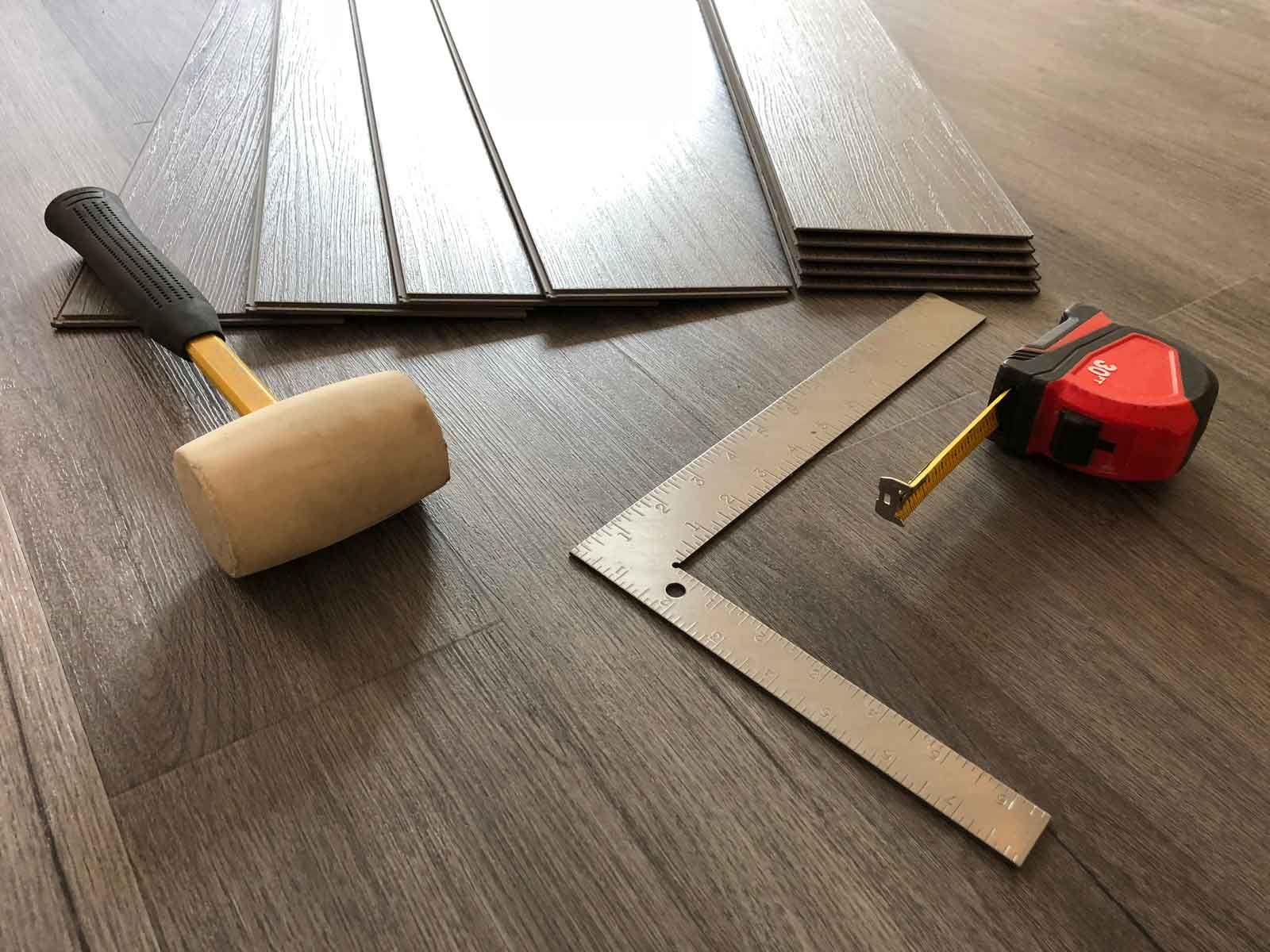 Flooring tools, planks, tape measure, mallet, and square on a wood floor.