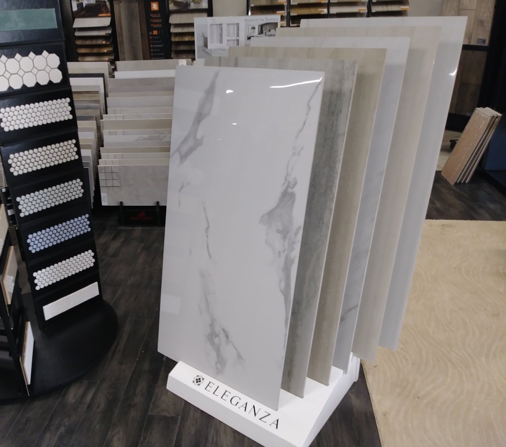 White marble-look tile samples on a showroom stand labeled “Eleganza”