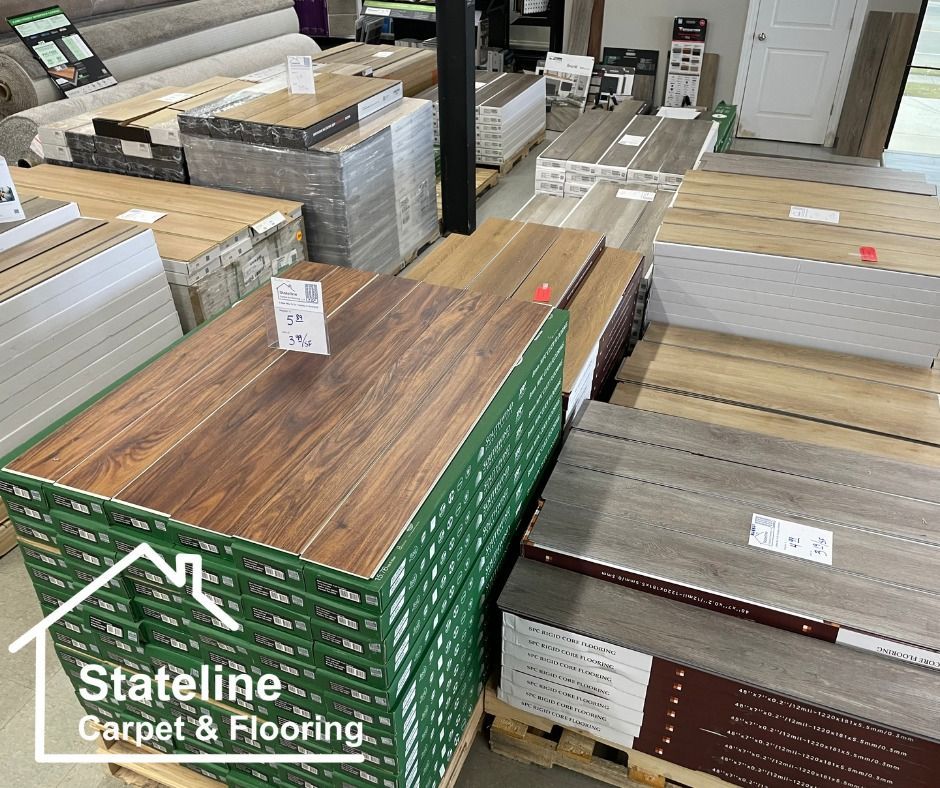 Flooring showroom with stacks of vinyl planks in wood and gray finishes, branded Stateline Carpet & Flooring.