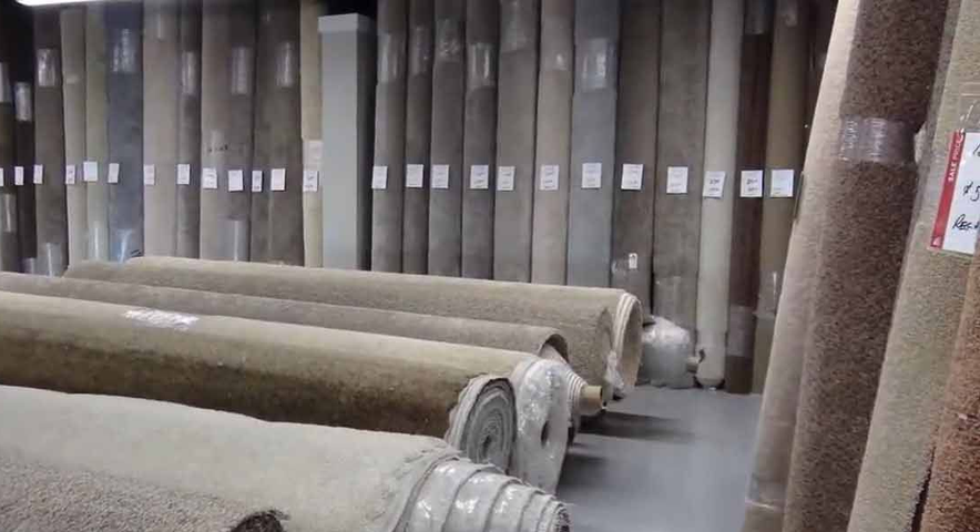 Rows of rolled carpets in a carpet warehouse, stacked upright and lying on the floor.