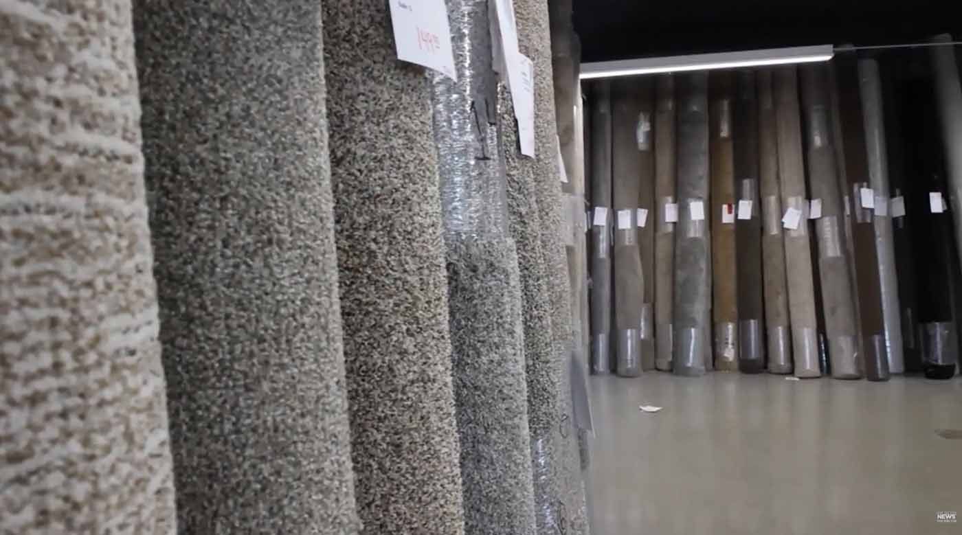 Rows of gray carpet rolls in a showroom, with curtains hanging in the background.