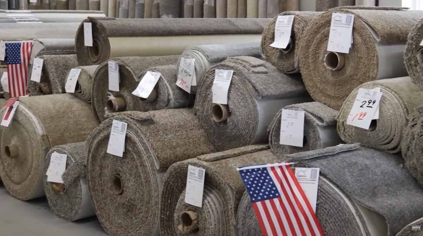 Rolled carpets stacked in a warehouse with small American flags attached to some rolls